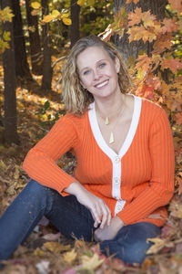 Portrait of smiling young woman sitting on tree trunk in forest