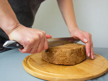 Hands cut with a knife brown cheese, norwegian brunost isolated on white background