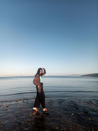 Full length of woman with arms outstretched standing at beach against clear sky