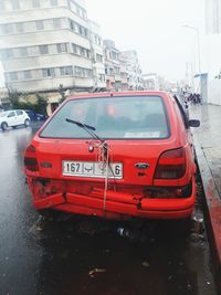 Red car on road by buildings in city