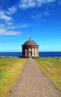 Tower on field by sea against blue sky