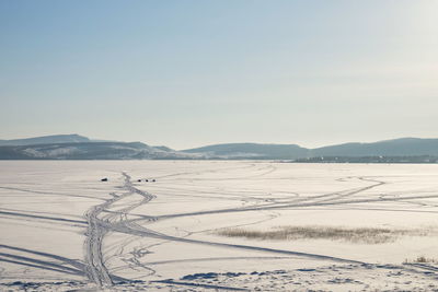 Fishermen catch fish on the great frozen lake, against the backdrop of the mountains, in winter.