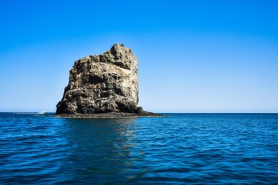 Rock formation in sea against clear blue sky