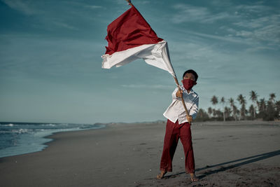 Full length of boy holding flag standing on beach against sky