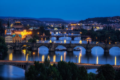 Illuminated bridge over river by buildings against sky at night