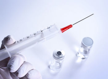 Cropped hand holding syringe by vial bottles against white background