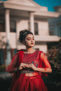 Young woman with red umbrella standing against built structure