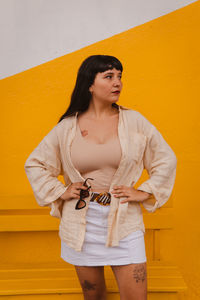 Dark-haired female model in vintage clothing and make-up against a colorful wall.