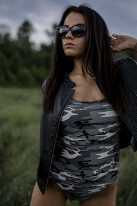 Sensuous young woman wearing camouflage bodysuit and leather jacket on field