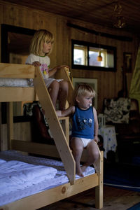 Brother and sister sitting on steps of bunkbed at home