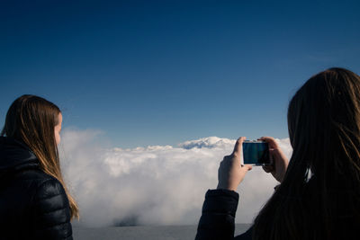 Rear view of woman photographing cloudy sky