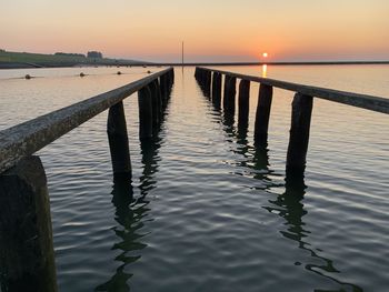 Wooden pier over sea against sky during sunset