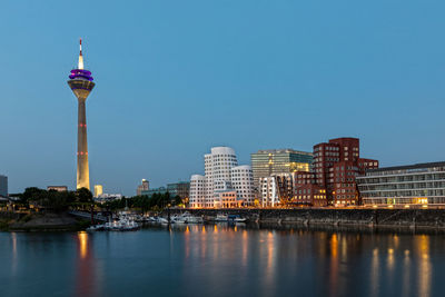 Illuminated buildings by river against sky in city