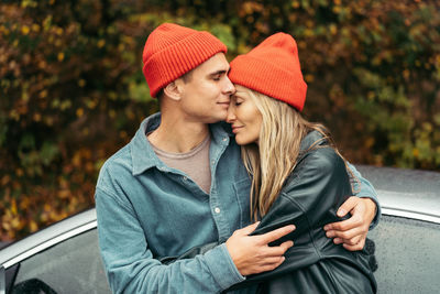 Young man and woman in red caps hugging outdoors in autumn.