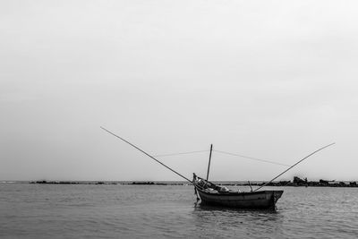 Sailboat fishing in sea against clear sky