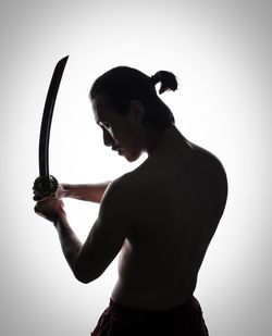 Shirtless mid adult man holding sword while standing against white background