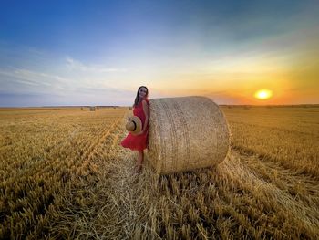 Man with hay bales on field against sky during sunset