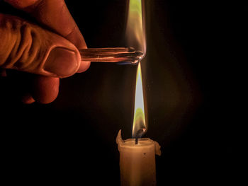 Close-up of hand burning candle against black background