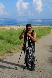 Man photographing through camera on road by sea against sky