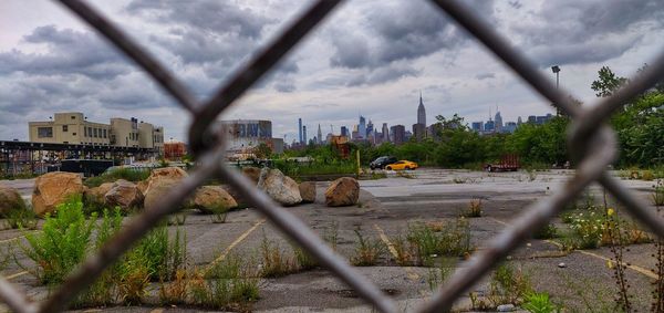 Panoramic view of buildings against sky seen through chainlink fence