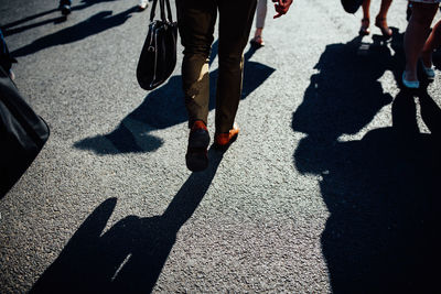 Low section of people walking on road during sunny day