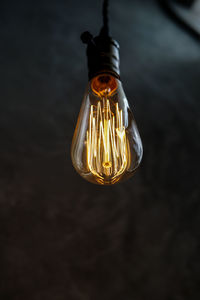 Low angle view of illuminated light bulb hanging against wall