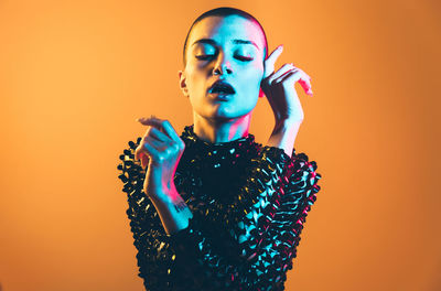 Portrait of young woman looking away against orange background