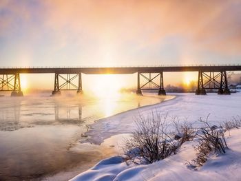Bridge over frozen lake against sky during sunset