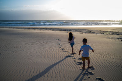 Rear view of kids on beach walking towards sunrise