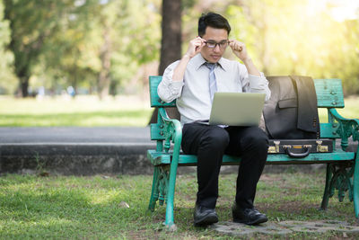 Businessman using laptop while sitting on bench in park