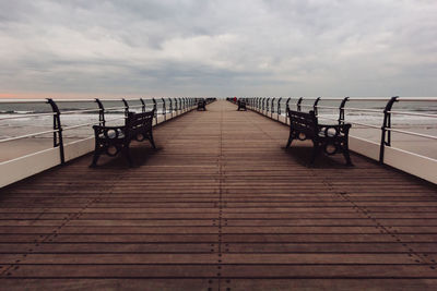 Wooden pier on sea against cloudy sky