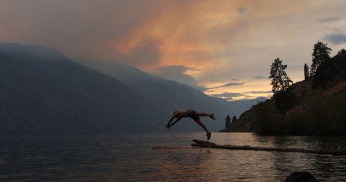 Rear view of man walking on lake against sky during sunset