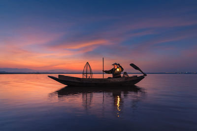 Fisherman in boat on lake against sky during sunset