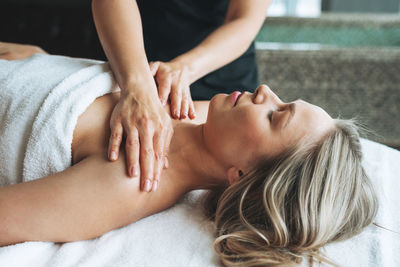 Attractive blonde young woman on couch with white linen enjoys hand facial massage in spa salon