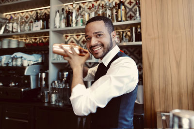 Smiling bartender shaking cocktail shaker at bar