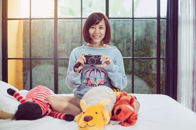 Portrait of smiling woman holding toy while relaxing on bed at home