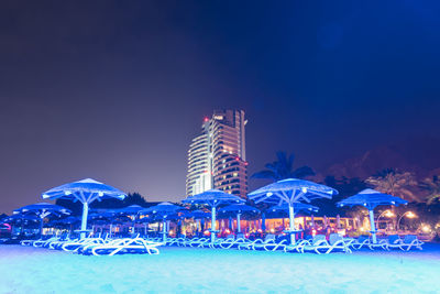 Illuminated ferris wheel by building against blue sky