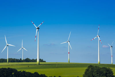 Windmills on field against blue sky