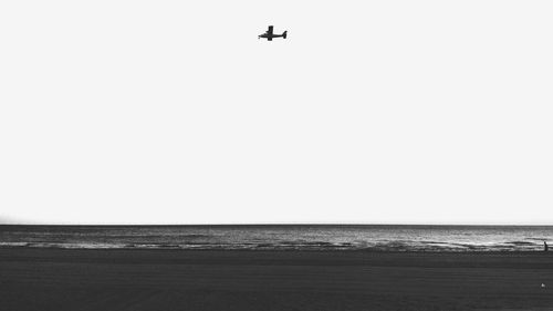 Scenic view of sea against airplane flying in clear sky