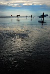 Silhouette people in sea against sky during sunset