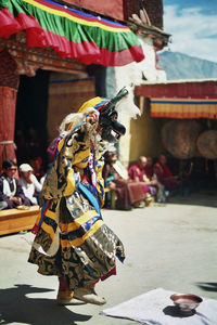 People looking at performer in costume dancing outside temple during festival