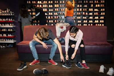 Teenage boy helping friend wearing shoes while sitting on sofa at bowling alley