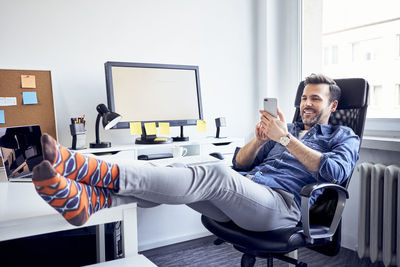 Relaxed man sitting at desk in office using cell phone