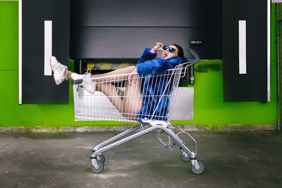 Side view of woman sticking out tongue while sitting in shopping cart