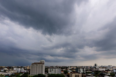 Buildings in city against storm clouds