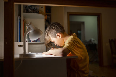 Student studying under desk lamp at home