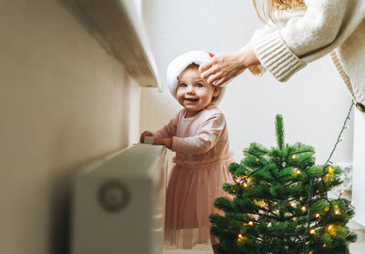 Cute little baby girl in pink dress and santa hat with her mother young woman in room at home