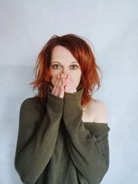 Portrait of mid adult woman with hands covering mouth standing against wall at home