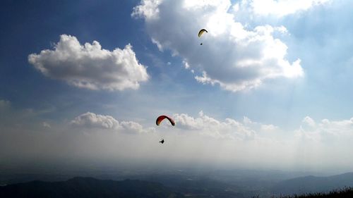 Low angle view of people paragliding against sky