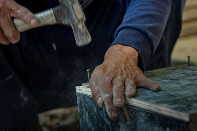 Midsection of man hammering nail on plank